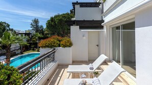 Un balcon avec deux fauteuils de jardin blancs, une petite piscine et un bâtiment blanc surmonté d’une pergola.