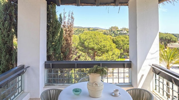 Un espace extérieur abrité, aménagé avec une table et des chaises, un lustre et offrant une vue sur un paysage verdoyant.