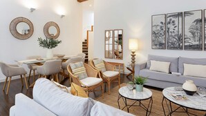 A modern living room with a sofa, two armchairs, a dining table with chairs, a coffee table, and a staircase.