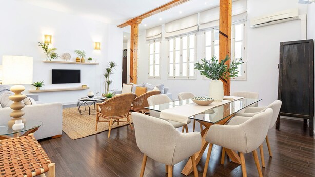 A modern living room with a glass dining table, white sofas, and wooden flooring.