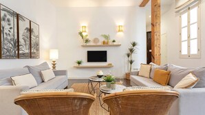 A modern living room with a sofa, two wicker chairs, a coffee table, and a TV on a wall-mounted shelf.