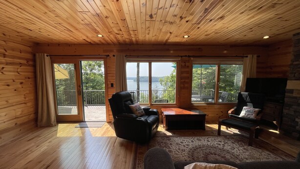 L’intérieur chaleureux d’un chalet avec des murs et des planchers en bois, une grande fenêtre offrant une vue imprenable, une cheminée et des sièges confortables.