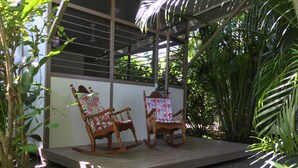 A wooden deck with two rocking chairs, surrounded by lush greenery and a white wall. - Eliott Jungle (Jaco)