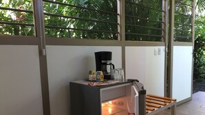 A compact kitchenette with a coffee maker, a small refrigerator, and a glass of water. - Eliott Jungle (Jaco)