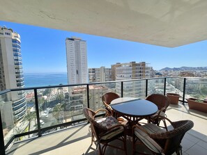 A balcony with wicker furniture and a glass table, overlooking a cityscape and the sea. - FRONT AL MAR LEVANTE BEACH R079 (Benidorm)