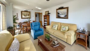 Ein Wohnzimmer mit blauem Sessel, beiger Couch und einem Holztisch.