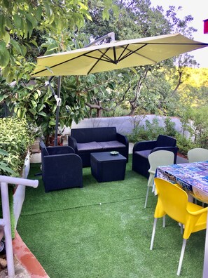 Une terrasse extérieure avec un parasol jaune, des meubles en osier noir et une table recouverte d’une nappe à motifs.