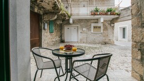 Un cortile con un tavolo rotondo e quattro sedie in vimini, una porta bianca e un balcone con piante in vaso.