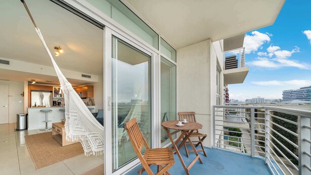 Een balkon met een hangmat, houten stoelen, een tafel en uitzicht op de stad.