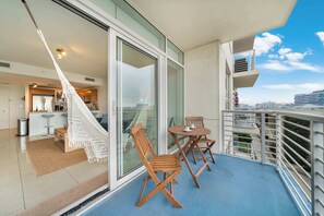 Un balcon avec un hamac, des chaises en bois, une table et une vue sur le paysage urbain.