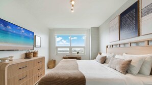Een slaapkamer met een bed, een dressoir, een televisie en een raam met uitzicht.