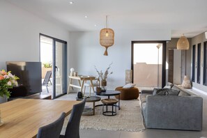 A modern living room with a wooden dining table, grey sofa, and a TV.