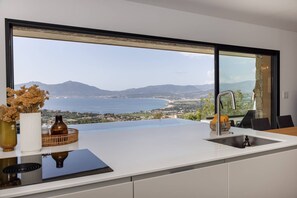 A kitchen with a large window overlooking a coastal landscape.