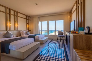 Een hotelkamer met een groot bed, een bureau en uitzicht op zee.