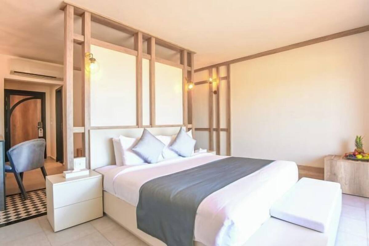 Un dormitorio moderno con una cama grande, mesitas de noche, una silla y una pequeña mesita con una planta.