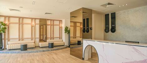 A spacious lobby with a reception desk, seating areas, and a large mirror reflecting the space.