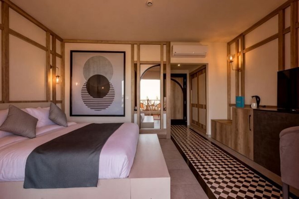 A hotel room with a bed, a television, a framed artwork, and a checkered floor.