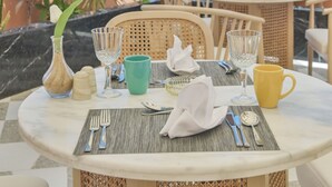 Une table ronde dressée pour deux personnes, avec vue sur la mer, agrémentée d’un luminaire suspendu et de plantes en pot.