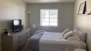 Une chambre à coucher avec un lit, une commode, un téléviseur, une lampe et une fenêtre.