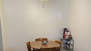 Un coin repas avec une table ronde en bois, six chaises et un ventilateur de plafond.