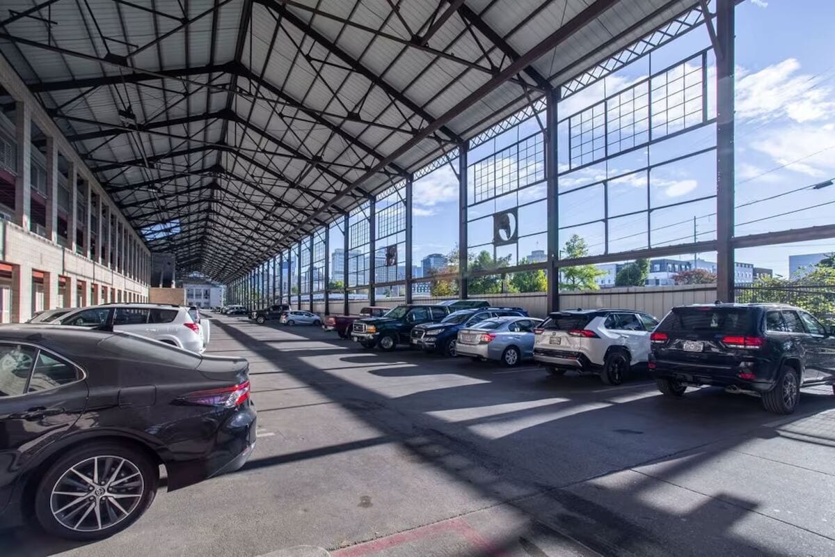 A covered parking area with multiple cars parked under a metal roof with large windows.