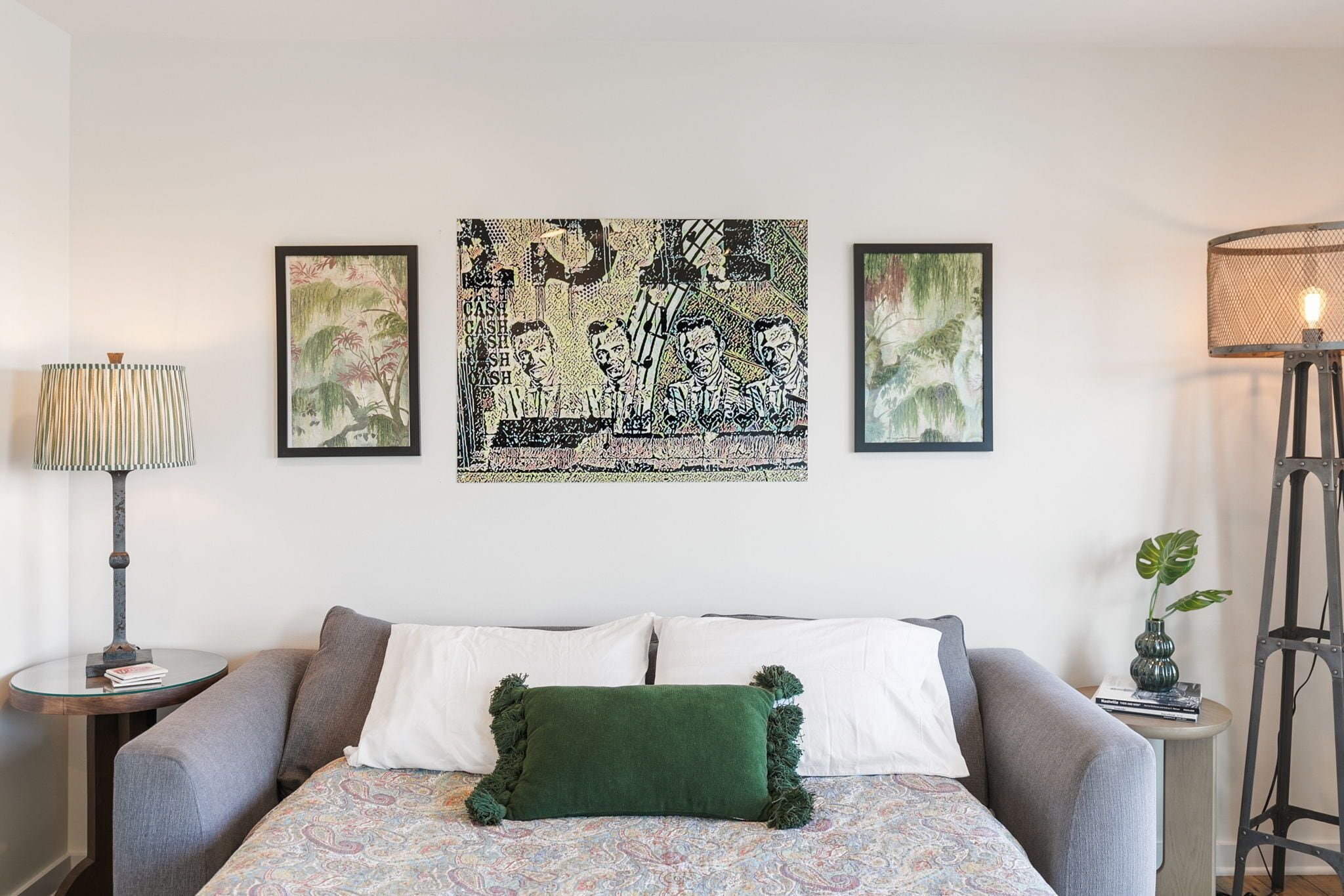 A bedroom with a bed, a side table, a lamp, and two framed artworks on the wall.