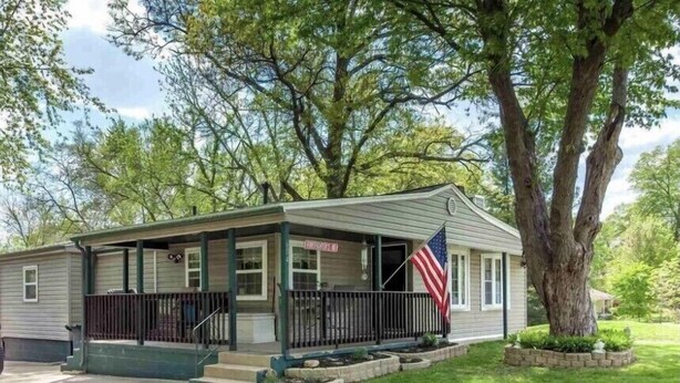 A single-story house with a front porch, a flag, and a large tree in the yard. - Home on the Green River! (Colona)