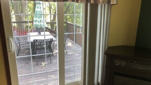 A sliding glass door leading to an outdoor deck with a table and chairs, a wooden deck, and a view of trees and a fence. - Home on the Green River! (Colona)