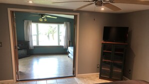 A bedroom with a bed, a television on a stand, and a sliding glass door leading to a balcony. - Home on the Green River! (Colona)