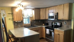 A kitchen with wooden cabinets, a stainless steel oven, a microwave, a sink, and a bar stool. - Home on the Green River! (Colona)
