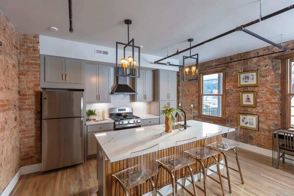 A modern kitchen with a large island, stainless steel appliances, and exposed brick walls.