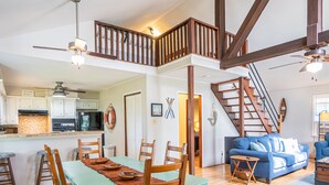 Ein geräumiger Wohnbereich mit Esstisch, Holzstühlen, einem blauen Sofa und einer Treppe, die zu einer oberen Ebene führt.