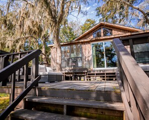 A wooden deck with a bench, a staircase, and a large window overlooking a wooded area. - Creekfront Cottage w/ Boat Lift & Pier (Sargent)