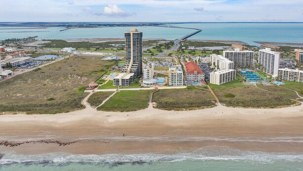 Un complejo turístico costero con propiedades frente a la playa, un puerto deportivo y un muelle destacado que se adentra en el agua.