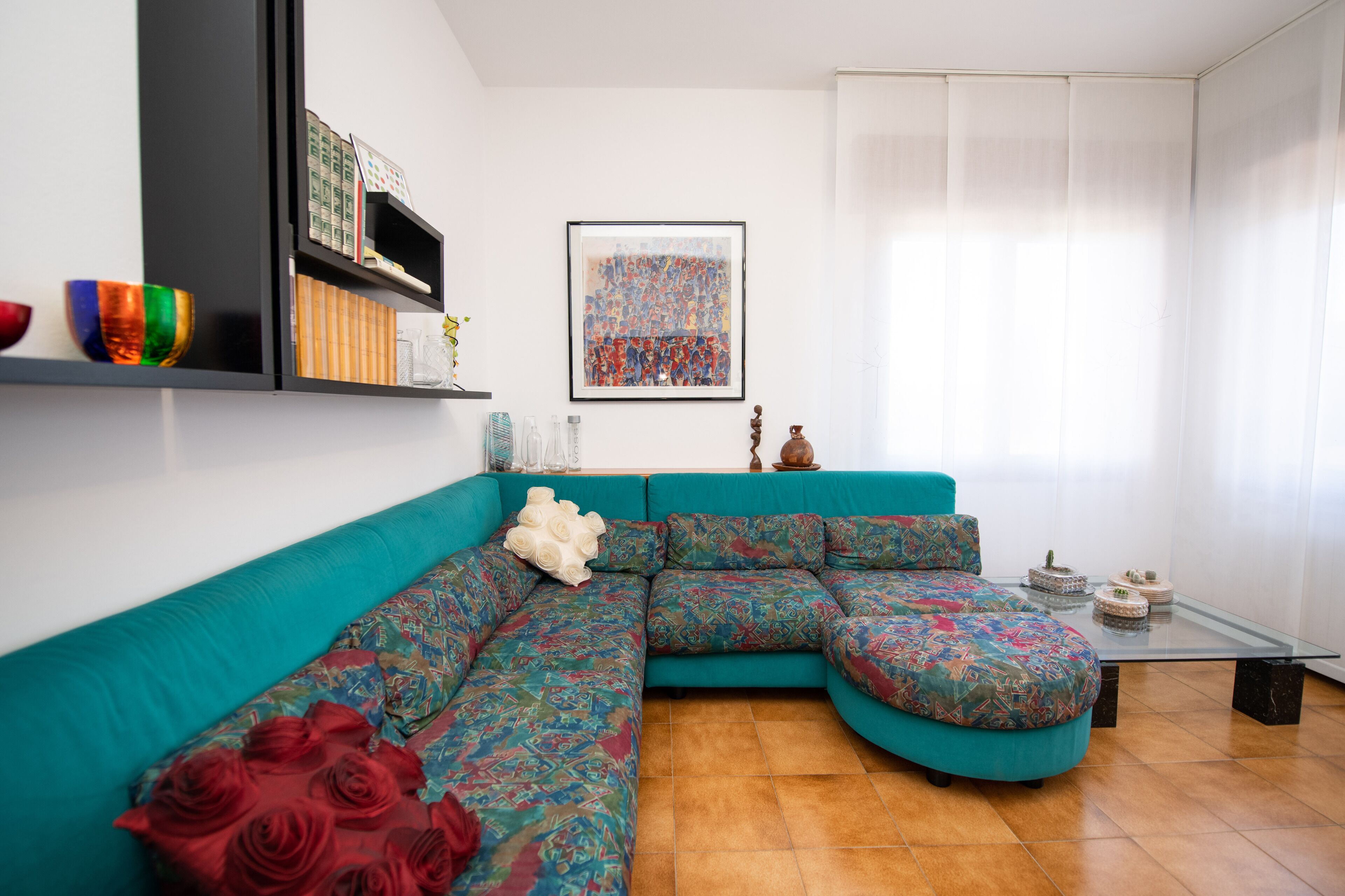 A modern living room with a teal sectional sofa, a glass coffee table, and a framed abstract painting on the wall.