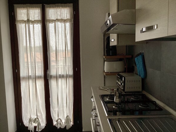 Una cocina con estufa, horno y microondas. Hay dos ventanas con cortinas de gasa.