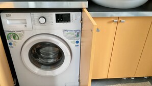 A front-loading washing machine with a digital display and control panel, located in a kitchen area with wooden cabinets and a tiled floor. - Peter's nest (Verano Brianza)