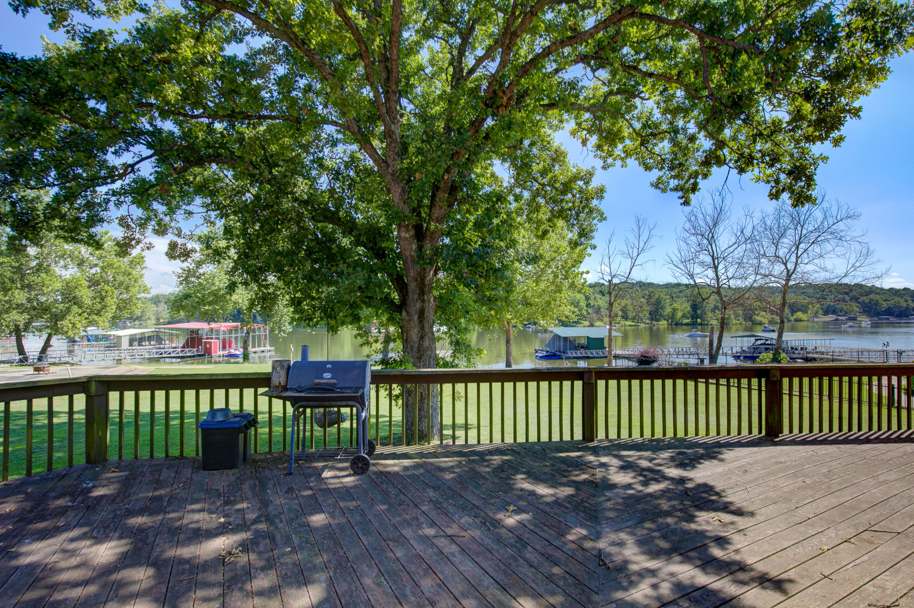 Una terraza de madera con una parrilla, un bote de basura y vistas a un lago con barcos.