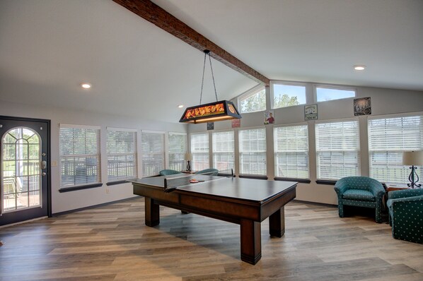 A spacious room with a pool table, comfortable seating, large windows, and a hanging light fixture. - Waterfront Home with private boat ramp and boat dock. (Grove)