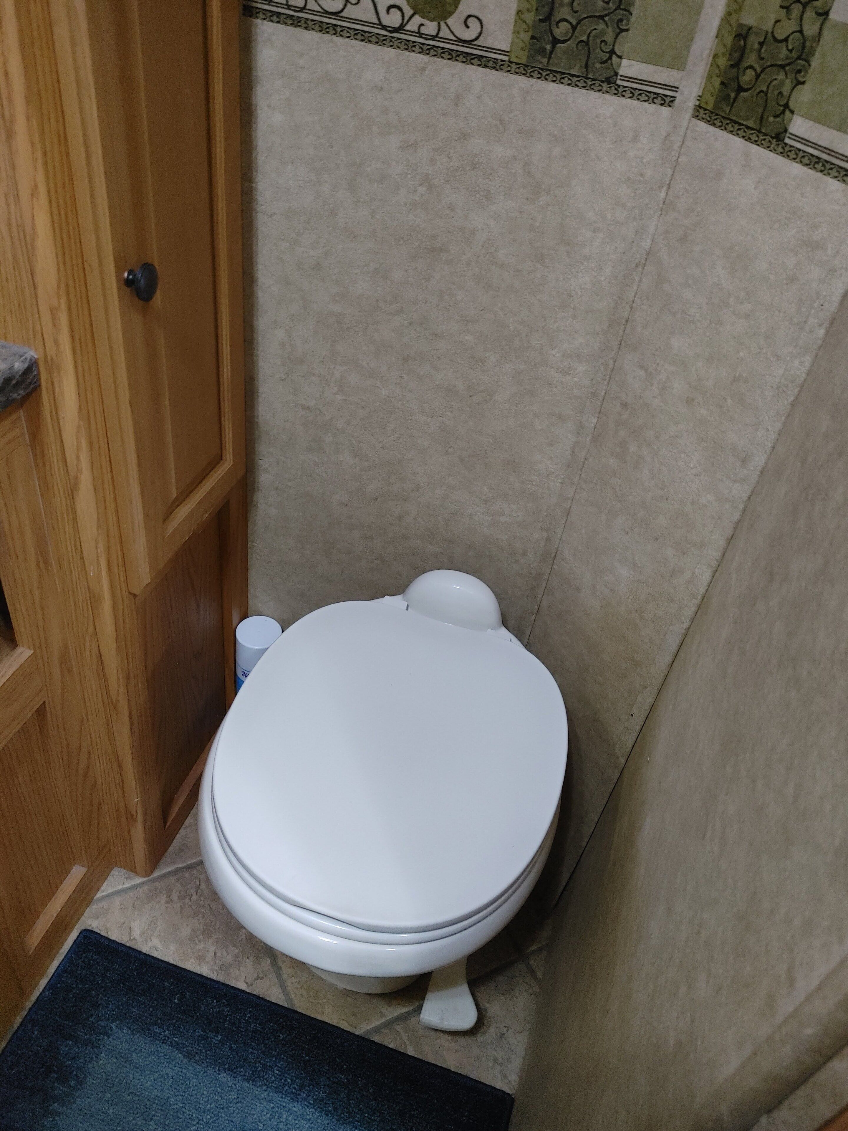 Un baño con inodoro blanco, puerta de madera y piso de baldosas.