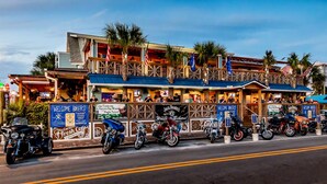 A waterfront restaurant with outdoor seating, multiple flags, and motorcycles parked outside. - RV NSB Sun & Shade Tree, Pool & Picnic RV Vacation (New Smyrna Beach)