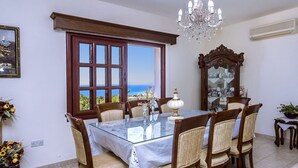 Un menjador amb taula de vidre, cadires de fusta, un candelabrum i vista al mar.