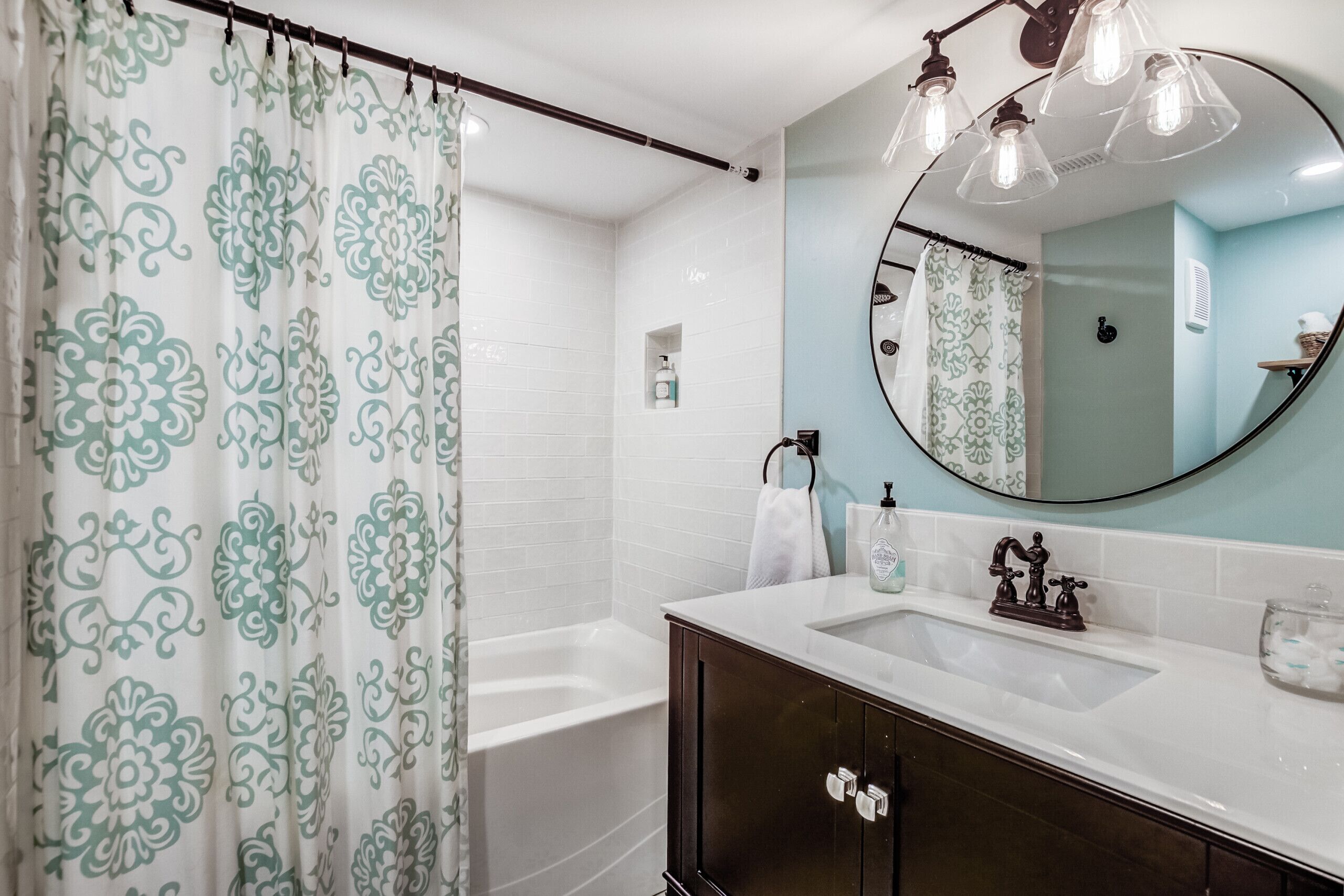 A bathroom with a shower curtain, a bathtub, a sink with a mirror, and a towel rack.