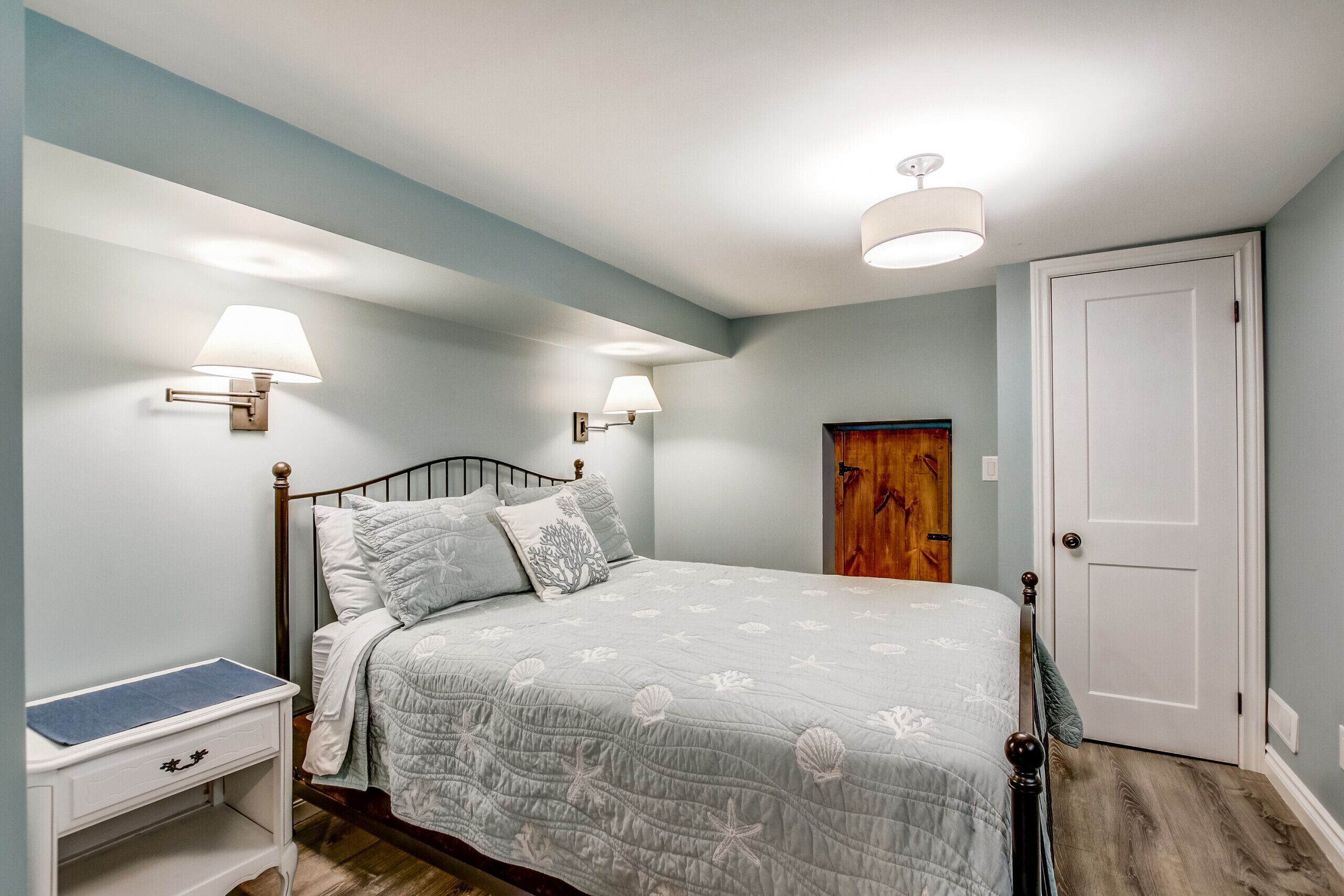 Une chambre à coucher comprenant un lit, des lampes de chevet, une table de chevet, une porte et une œuvre d’art accrochée au mur.