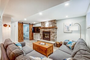 A living room with a stone fireplace, grey sofas, a wooden coffee table, and a television mounted on the wall. - Blue Pearl, Your Tranquil Oasis (Niagara-on-the-Lake)