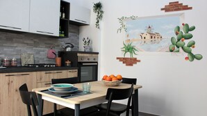 A modern kitchen with a dining table, chairs, and a wall mural. - Suite Torre Pali (Trapani)