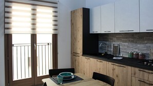 A modern kitchen with wooden cabinets, a black countertop, and a window with blinds. - Suite Torre Pali (Trapani)