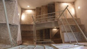 A staircase with a metal handrail and stone steps, surrounded by walls with recessed lighting. - Suite Torre Pali (Trapani)