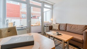 A modern living room with a sofa, a small table, and a chair. Large windows offer a view of the outside.
