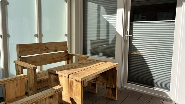 A wooden bench and table set on a wooden deck with a glass door and window.